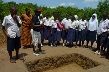 Figure 6: UDSM student Verynice Mtaki explaining to primary student about the whole process of excavation and its importance in revealing the history of the area. Photo credit Elinaza Mjema.